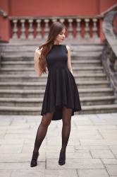 Czarna sukienka z dłuższym tyłem, czarne pończochy oraz lakierowane szpilki